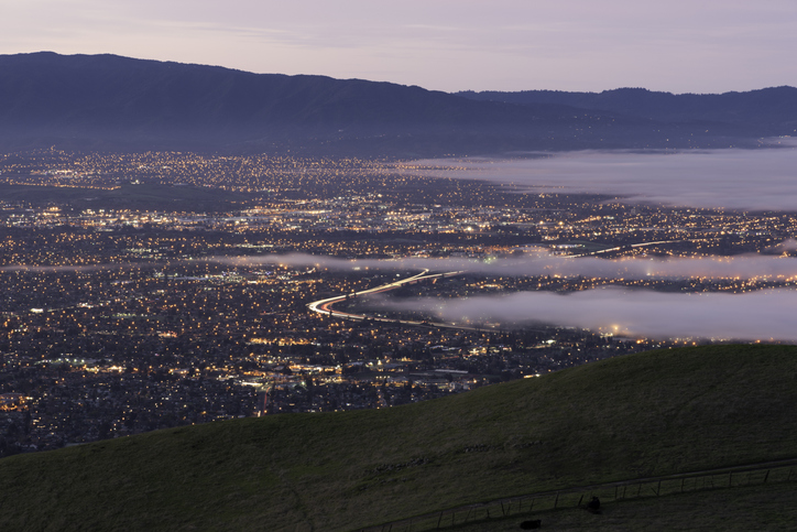 A early morning fog rolls into San Jose Calif. Typical late summer, early fall morning. The heat in the Central Valley pulls the fog in through the Golden Gate overnight and the fog slowly makes its way up valley covering the city for the morning commute. The I680 corridor is seen as the bending line of lights near the center of the picture.